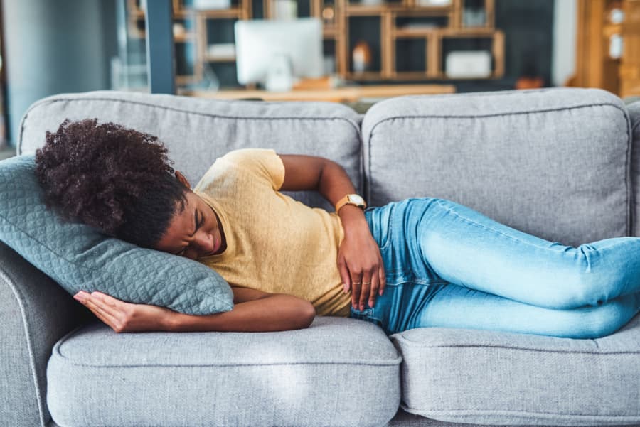 Young Woman Laying On Couch Holding Stomach