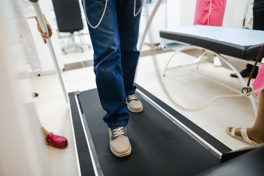 Male patient’s legs shown during a cardiac stress test on a treadmill at clinic