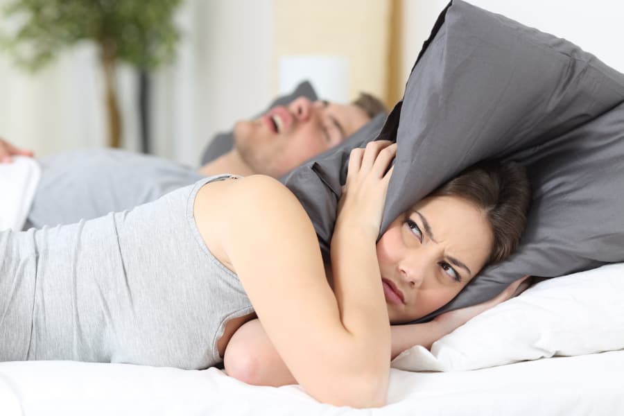 Woman covers ears with pillow as partner snores