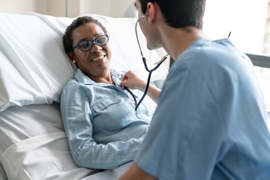 Nurse listens to smiling patient’s chest with stethoscope