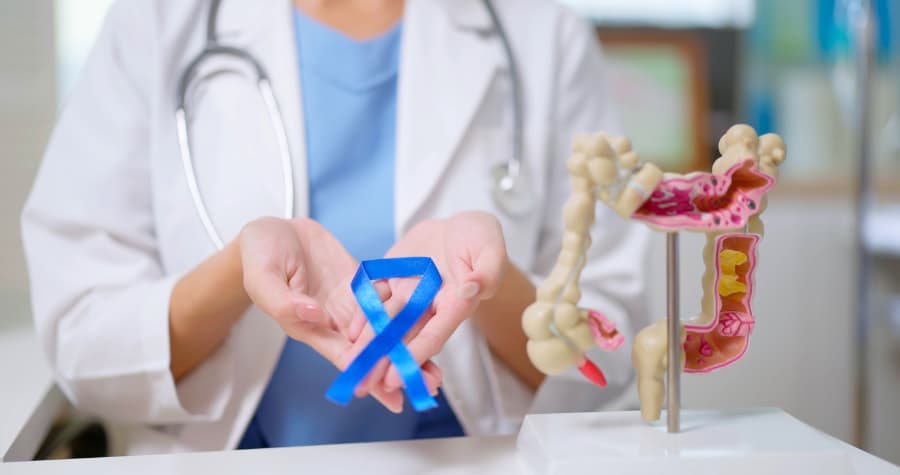 Closeup of physician holding colon cancer ribbon next to model of colon