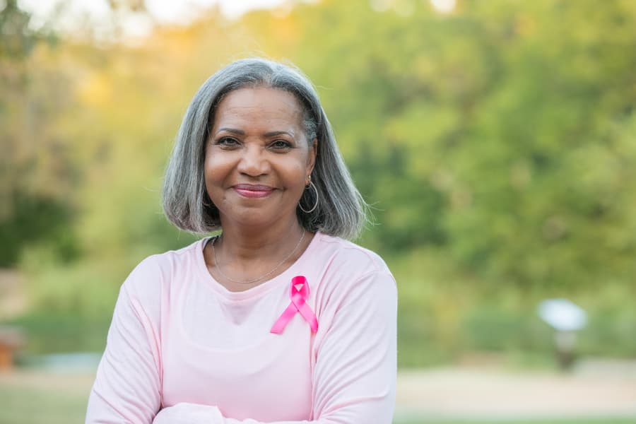 Older woman smiling while wearing pink breast cancer ribbon