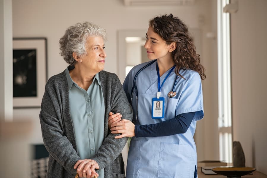 Caregiver assists senior woman with walking at home