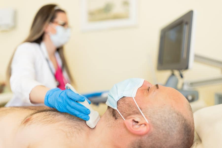 Medical technician watches screen while performing ultrasound scan on patient’s neck