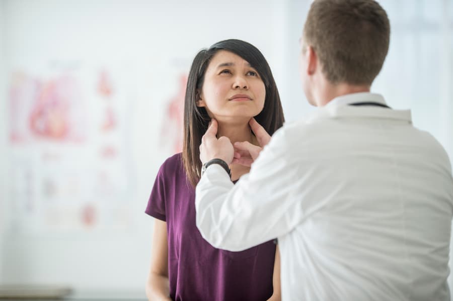 Physician places hands on patient’s throat to examine thyroid gland