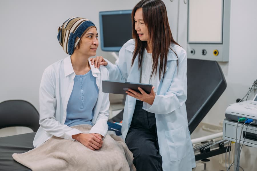 Doctor with clipboard discusses breast cancer treatment with patient in hospital room 