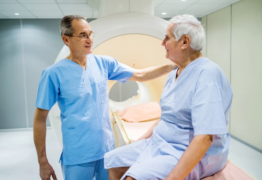 Radiation oncologist pats patient on shoulder prior to lying down in MRI machine