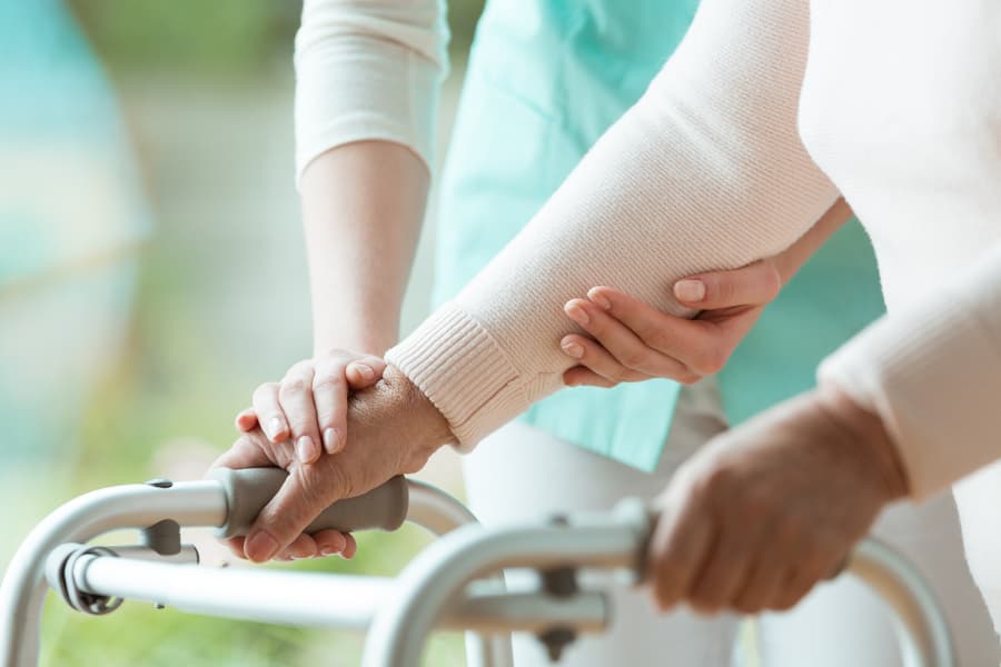 Nurse assists Parkinson’s patient with metal walker
